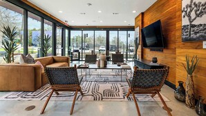 A modern living room with a large TV, comfortable seating, and a view through large windows. - South Lamar Condo / Sauna / Cold Plunge / Pickleball (Austin)