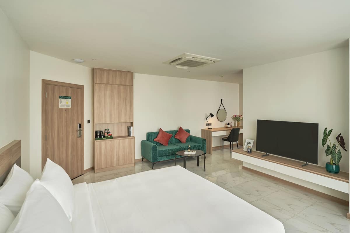 A hotel room with a bed, a desk, a TV, a coffee machine, and a plant.