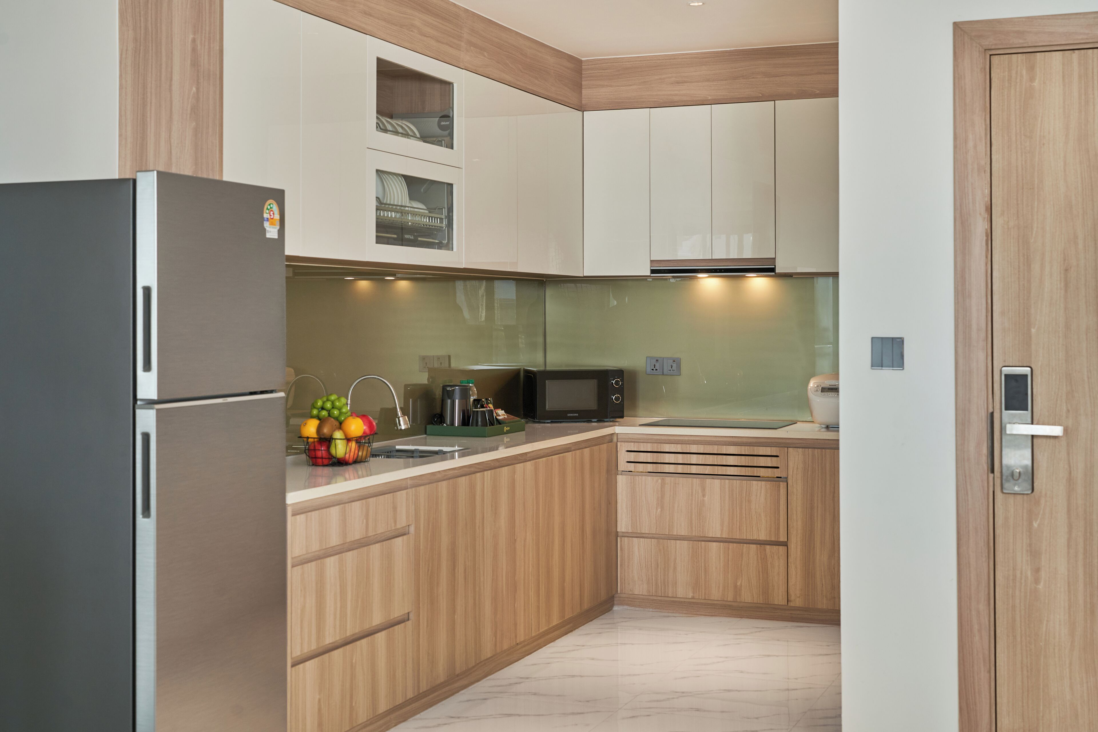 A modern kitchen with wooden cabinets, a stainless steel refrigerator, a microwave, and a sink.