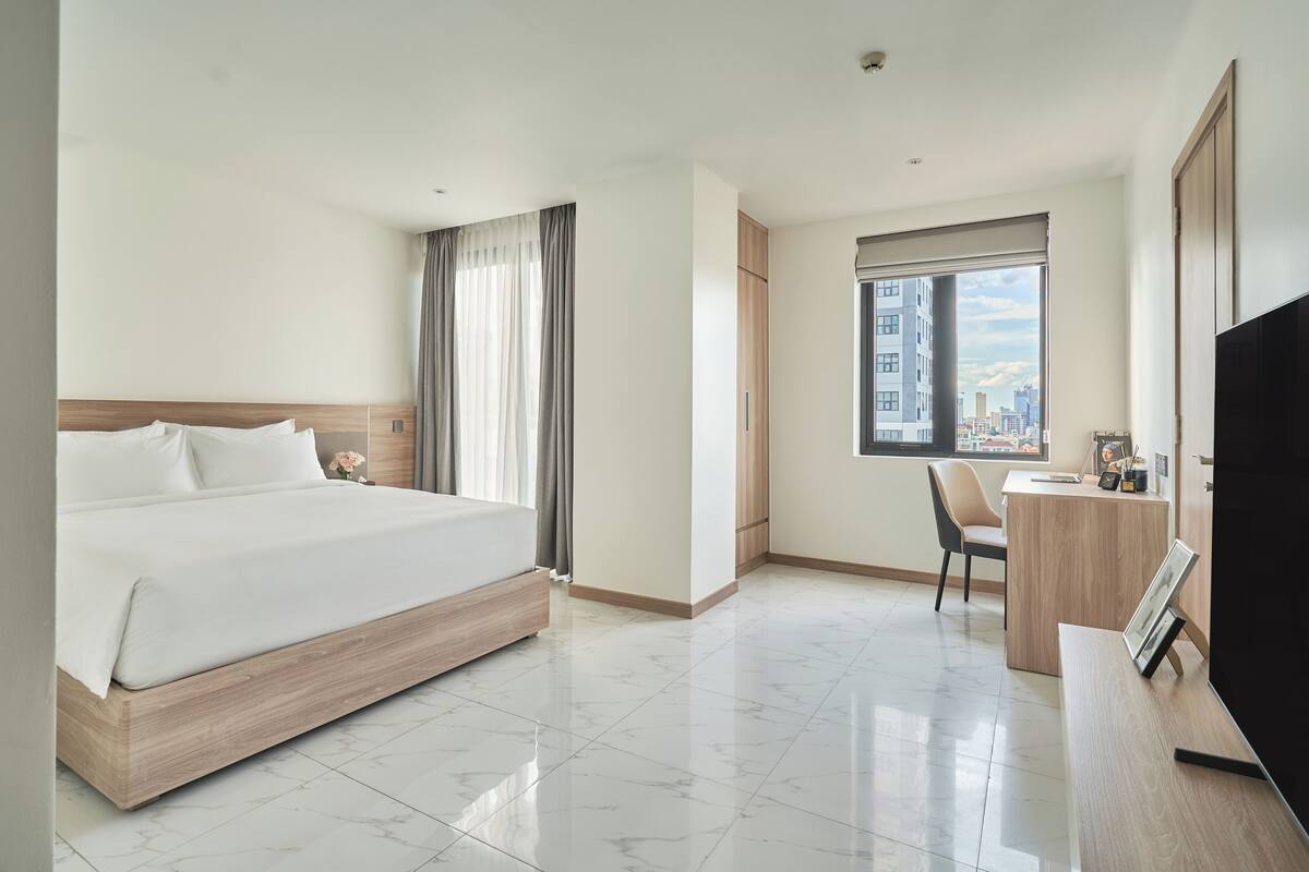A modern hotel room with a large bed, a desk, and a TV.
