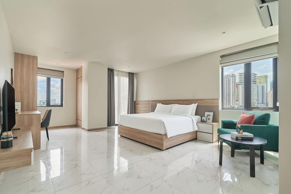 A modern hotel room with a large bed, a TV, a desk, and a sofa.