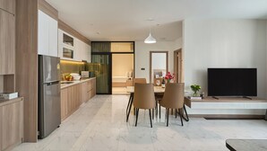 Une cuisine moderne équipée d’un réfrigérateur, d’un four à micro-ondes et d’un évier intégrés. On y trouve également un coin repas avec une table et des chaises, ainsi qu’un téléviseur à écran plat posé sur un meuble.