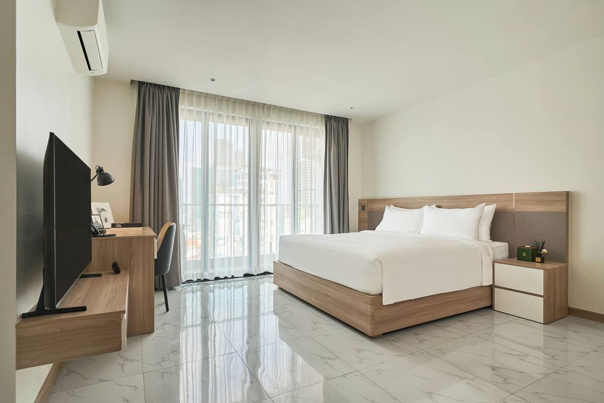 A modern hotel room with a large bed, a desk with a computer, and a TV.
