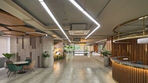 Un espace d’accueil moderne, doté d’un comptoir de réception en bois, d’un coin salon avec une table ronde et des chaises, et offrant une vue sur un escalier menant à un étage supérieur.