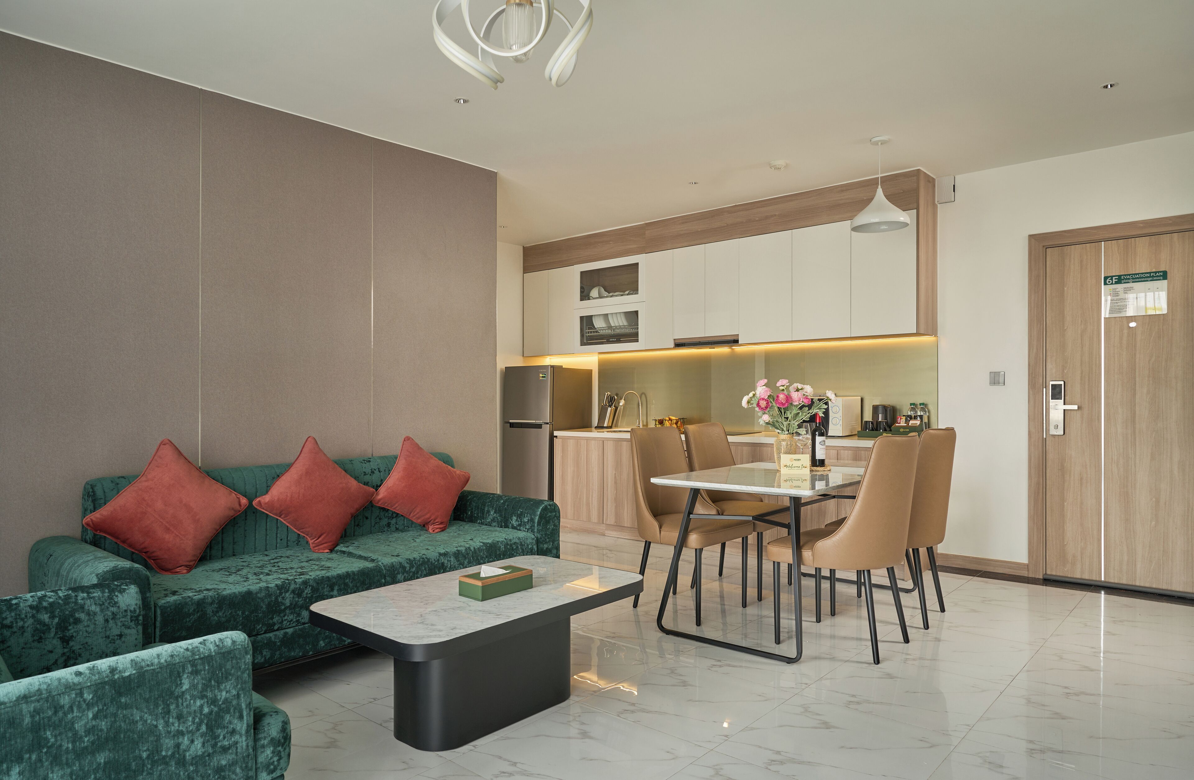 A modern living room with a green sofa, red cushions, a coffee table, and a dining area with chairs and a table.