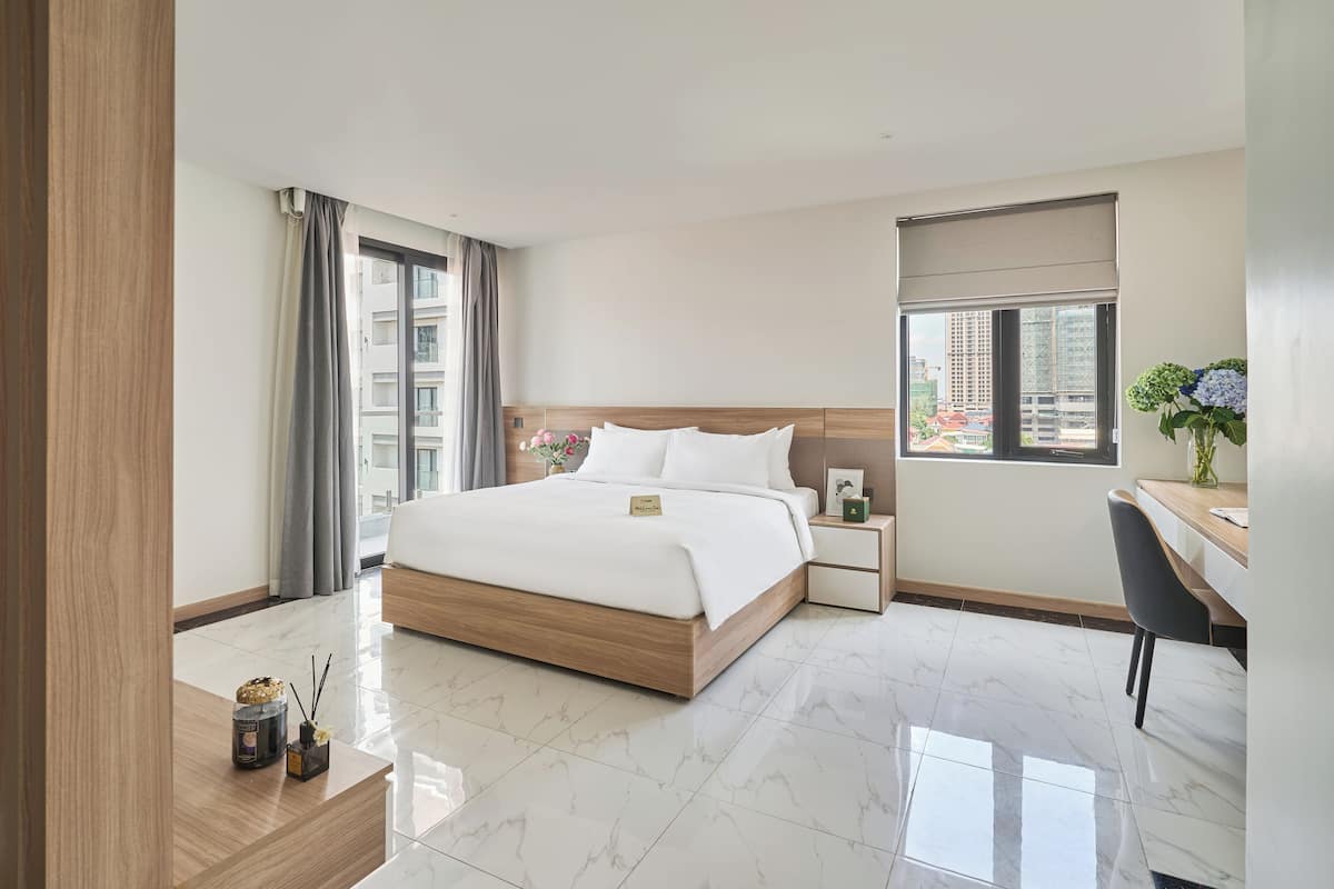 A modern hotel room with a large bed, a desk, and a window with a city view.