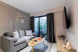 A modern living room with a grey sofa, a wooden coffee table, a flat-screen TV, and a large window with curtains.