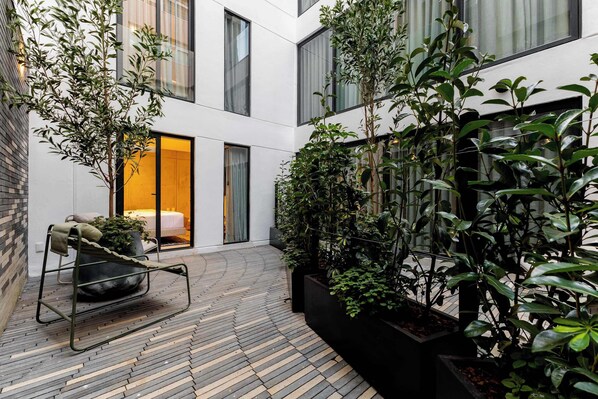 A modern building with a courtyard, potted plants, and a metal chair.