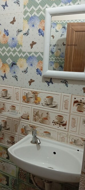 Ein Badezimmer mit Waschbecken, Spiegel und Wandgestaltung mit Schmetterlingsmustern und Kaffeetassen-Motiven.