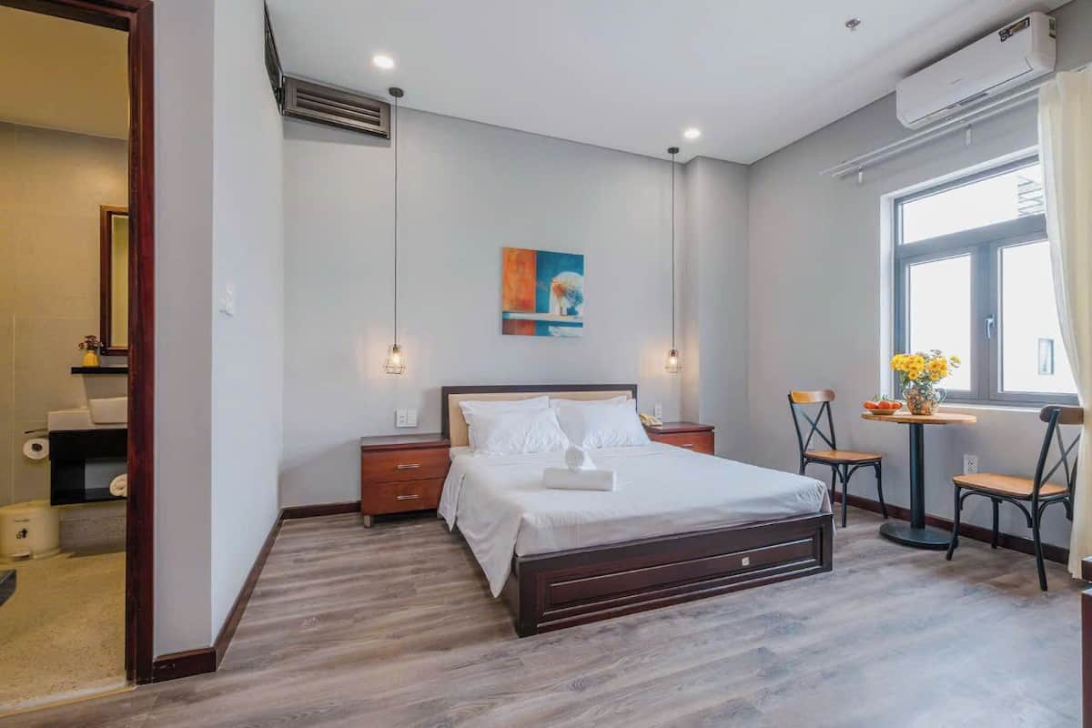 A modern bedroom with a large bed, bedside tables, a small table with chairs, and a window with curtains.