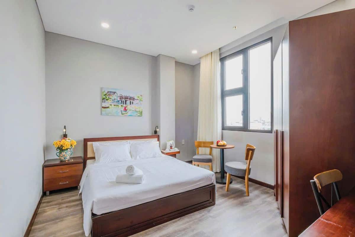 A hotel room with a bed, a small table, two chairs, a window, and a painting on the wall.