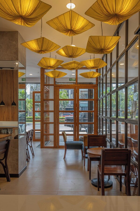 A restaurant interior with wooden furniture, large windows, and hanging yellow lamps. - River Light Condotel (Da Nang)