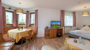 A cozy room with a dining table, a sofa, a TV, and a bed. - Apartment type 4 (Anger)