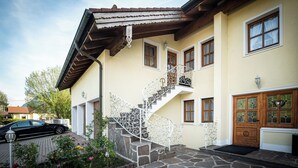 A two-story house with a stone staircase, a wooden door, and a car parked in the driveway. - Apartment type 4 (Anger)