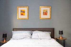 A hotel room with a bed, two framed artworks on the wall, and two bedside lamps.