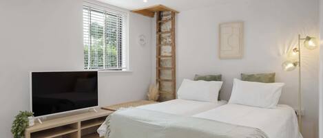 A bedroom with a bed, a TV on a wooden stand, a window with blinds, a ladder, a wall-mounted light fixture, and a small plant.