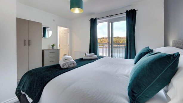 A modern hotel room with a large bed, a wardrobe, a mirror, and a view of the outdoors through a window. - Staithes House (Gateshead)