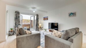 A living room with a sofa set, a flat-screen TV, and a view of the outdoors through a sliding door. - Staithes House (Gateshead)
