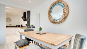 A modern kitchen with white cabinets, a wooden dining table, and a round mirror with a rustic frame. - Staithes House (Gateshead)