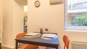 A dining area with two tables set for two, each with plates, cutlery, and a wine glass. A clock is on the wall, and a window provides a view of the outside. - Grece - centre ville - proche des commodités (Toulouse)
