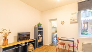 A compact living space with a TV, bookshelf, dining table, and chairs. A washing machine is visible in the background. - Grece - centre ville - proche des commodités (Toulouse)