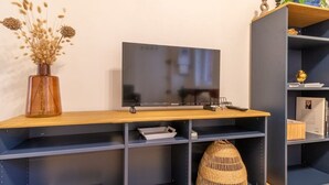 A modern living room with a flat-screen TV on a wooden TV stand, a dark blue bookshelf, and a decorative vase with dried flowers. - Grece - centre ville - proche des commodités (Toulouse)