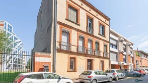 A multi-story building with a beige facade, multiple balconies, and a parking lot with several cars. - Grece - centre ville - proche des commodités (Toulouse)