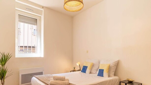 A bedroom with a bed, bedside table, lamp, and a window with blinds. - Grece - centre ville - proche des commodités (Toulouse)