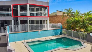 A hotel with a rooftop pool, a two-story building, and a fenced area with palm trees. - Beachside 2-Bed Apt in Hervey Bay with Parking (Torquay)