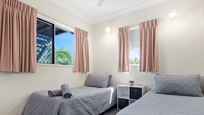 A bedroom with two beds, a nightstand, and a window with curtains. - Beachside 2-Bed Apt in Hervey Bay with Parking (Torquay)