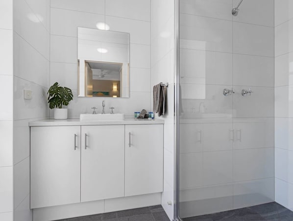 A modern bathroom with a glass shower enclosure, white cabinetry, and a potted plant.