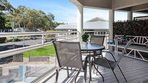 An outdoor balcony with a table and chairs, a view of a road, and a building in the background. - Beachside 2-Bed Apt in Hervey Bay with Parking (Torquay)