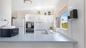 A modern kitchen with white cabinetry, a built-in oven, a microwave, and a large island with a sink. - Beachside 2-Bed Apt in Hervey Bay with Parking (Torquay)