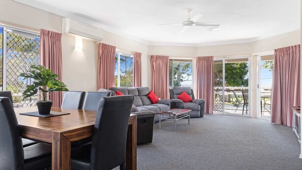 A spacious room with a dining area, seating, and a ceiling fan. - Beachside 2-Bed Apt in Hervey Bay with Parking (Torquay)