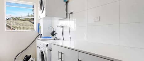 A laundry room with a washing machine, a dryer, and a hose. There is a window with a view of a building outside.