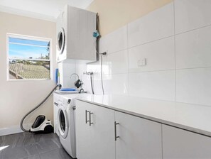 A laundry room with a washing machine, a dryer, and a hose. There is a window with a view of a building outside.