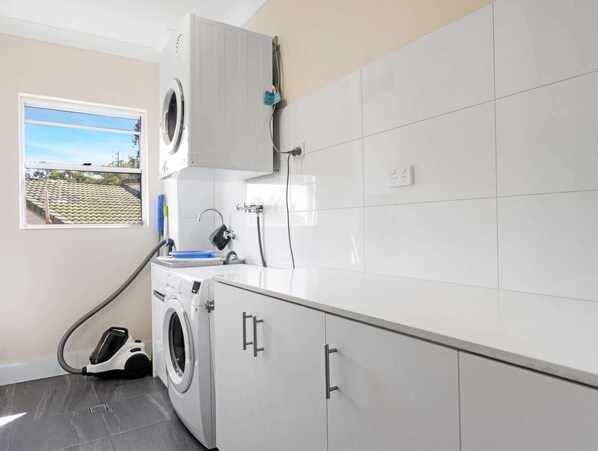 A laundry room with a washing machine, a dryer, and a hose. There is a window with a view of a building outside.