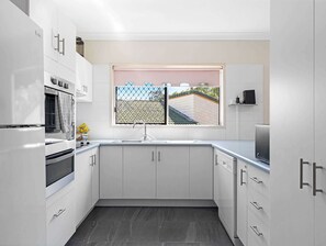 A modern kitchen with white cabinetry, a stainless steel sink, and a window with a view of a roof.