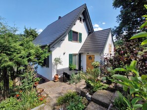 A house with a sloped roof, a front door, and a small porch area with potted plants and a table. - Black Forest Queen House (Bühlertal)