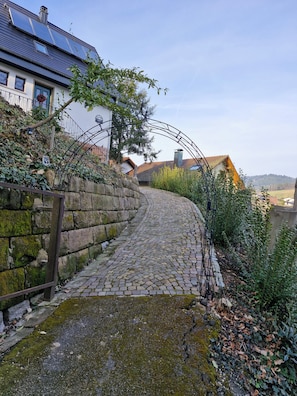 A cobblestone pathway leading to a house with a blue door, surrounded by greenery and a stone wall. - Black Forest Queen House (Bühlertal)