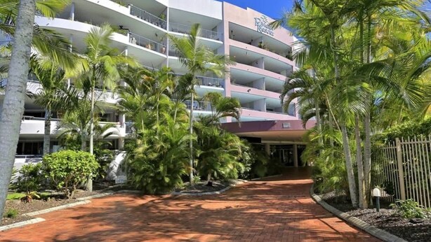 A multi-story hotel with a central atrium, surrounded by palm trees and a brick pathway. - Hervey Bay Resort Stay with Balcony & Parking (Torquay)