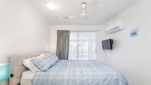 A bedroom with a bed, a ceiling fan, a TV mounted on the wall, and a window with curtains. - Hervey Bay Resort Stay with Balcony & Parking (Torquay)