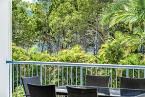 Varanda com mesa e cadeiras, vista para um jardim exuberante com diversas árvores e plantas.