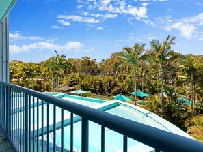 Área de piscina com vista para uma paisagem tropical, incluindo palmeiras e um céu claro.