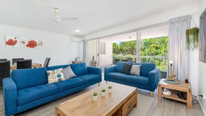 A modern living room with two blue sofas, a wooden coffee table, and a ceiling fan. - Hervey Bay Resort Stay with Balcony & Parking (Torquay)