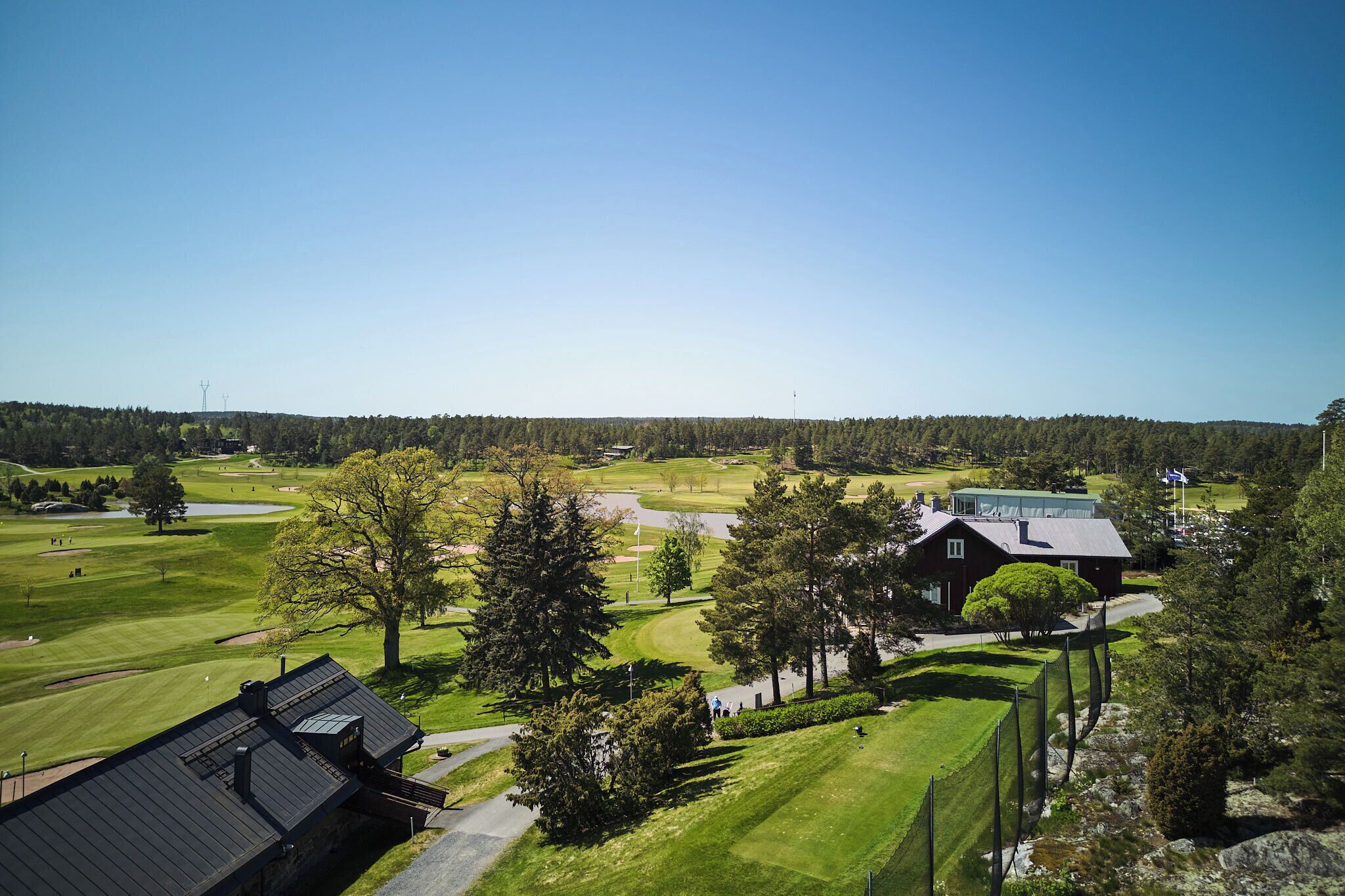 A golf course with a clubhouse, surrounded by trees and a clear sky.