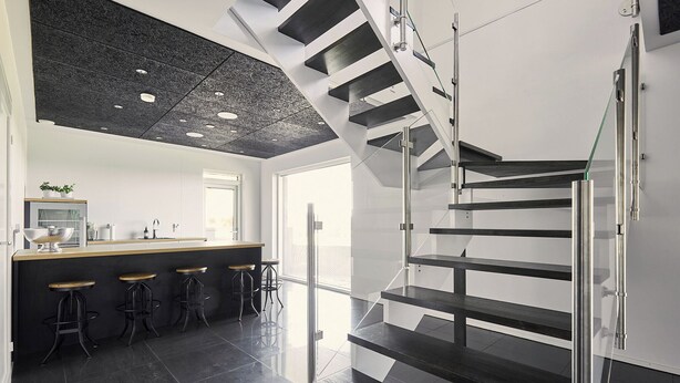 Eine moderne Küche mit einer zentralen Kochinsel, Barhocker und einer Treppe mit Glasgeländern.