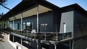 Ein modernes Gebäude mit einer überdachten Außenfläche, großen Fenstern und einem Glasgeländer.