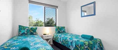 Un dormitorio con dos camas, una ventana con vistas, un ventilador de techo y un espejo en la pared.
