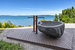 A wooden deck with a stone basin and metal structure, overlooking a body of water. - Stylish Home with Outdoor Area & Spectacular Views (Penna)